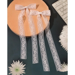 Detailed view of white embroidery lace bow hair clips with long ribbons on wooden tray