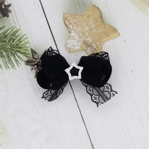 Dettaglio del fermaglio vintage in pizzo nero con stella di strass su legno bianco