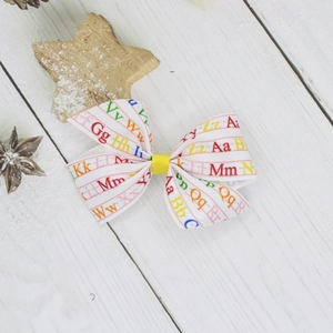 Detail of white bow hair clip featuring colorful alphabet letters on a wooden background