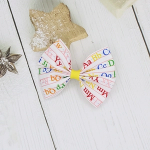 Detailed macro view of ABC alphabet print hair bow on a rustic white wood texture