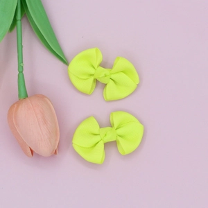 Detail of neon yellow ribbed ribbon hair bows placed on a pink background with a tulip