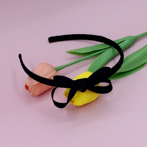 Close-up of a black grosgrain bow headband on a pink backdrop with tulips
