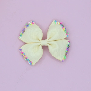 Detail view of beige ribbed grosgrain hair bow clip with colorful candy sprinkle accents