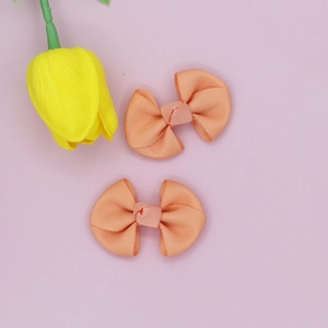 Detail of coral pink ribbed bow hair clips set on a clean pink background with tulips
