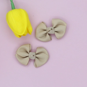 Detail view of beige grosgrain ribbon bow clips on a soft pink background with a tulip