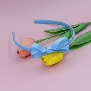 Detailed close-up of sky blue ribbed grosgrain bow headband on pink background