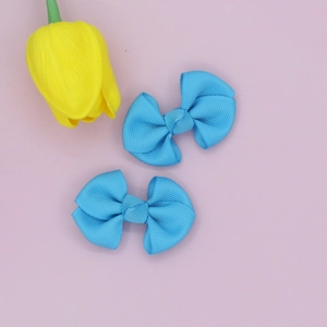 Flat lay of two bright blue grosgrain ribbon bow hair clips on a purple background
