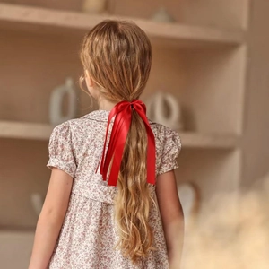 Détail d'un nœud en ruban de satin rouge porté par une fille blonde en robe fleurie