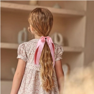 Élastique à cheveux élégant en satin rose avec long ruban porté par une fille en intérieur