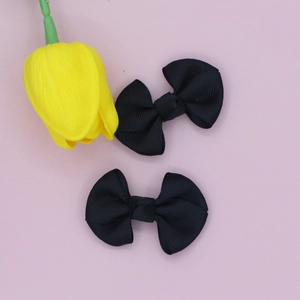 Detail view of a pair of black grosgrain ribbon bow hair clips on pink background