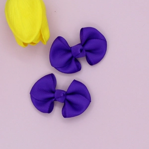 Close-up of a pair of deep purple ribbed grosgrain bow hair clips on pink background