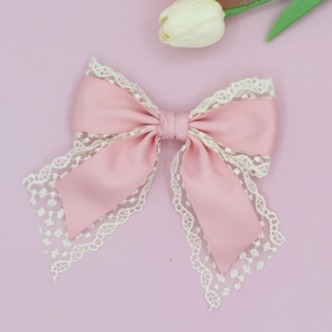 Detail of pink satin bow hair clip with white lace trim and flowing ribbons