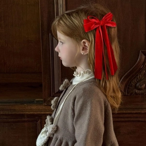 Detail of red velvet bow hair clip with long ribbons worn by a young girl for a vintage look