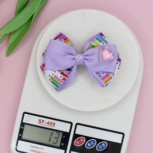 Lilac school pencil bow hair clip for girls with a pink heart detail on a white scale