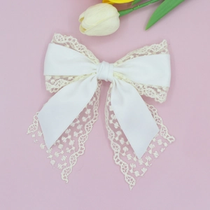 Detail view of white lace and satin bow hair clip on a soft pink background with tulips