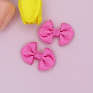 Detail of two rose red grosgrain ribbon bow hair clips with ribbed texture on pink background