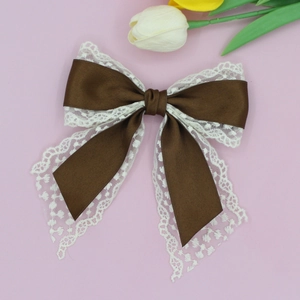 Detail of the brown satin ribbon and white lace bow hair clip on a pink surface