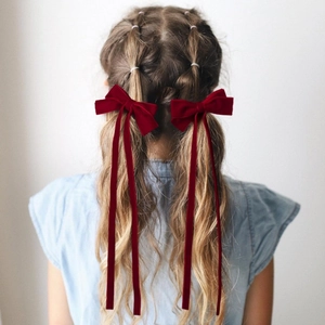 Détail de pinces à cheveux avec nœuds en velours rouge foncé et rubans sur tresses