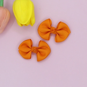Detail of two orange grosgrain ribbon bow hair clips on a soft floral background