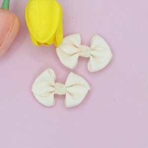 Close-up of cream-colored ribbed fabric bows with elegant knot detail on pink background