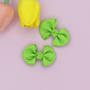 Detailed close-up of two grass green ribbed ribbon bow hair clips on a flat surface