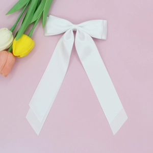 Détail d'un nœud papillon en satin blanc avec longs rubans sur fond de tulipes roses