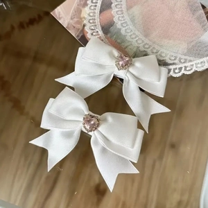 Detailansicht der weißen Satin-Haarschleifen mit rosa Herzkristall und funkelnden Strasssteinen