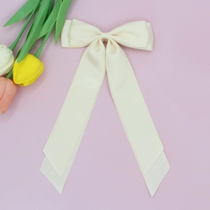 Détail d'un nœud papillon en satin crème avec de longs rubans sur fond rose doux