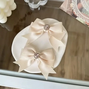 Paar cremefarbene Satin-Schleifen-Haarspangen mit Herz-Strass auf dekorativem Keramiktablett