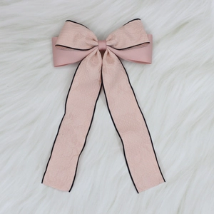 Detail of pink bow hair clip with black piping and jacquard texture on white plush