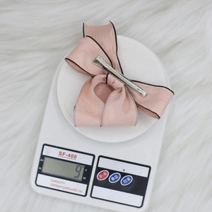 Pink bow hair clip with black trim on a scale weighing 9g for a lightweight accessory