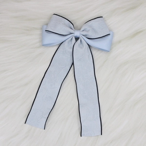 Detail of light blue bow hair clip with jacquard texture and long ribbons on plush background