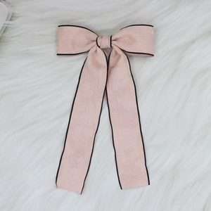 Detail of elegant pink bow hair clip with textured floral jacquard and black piped edges