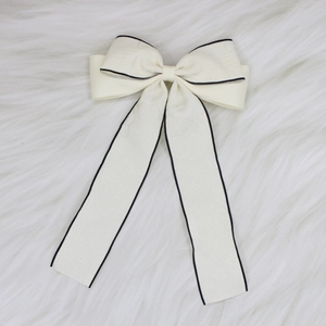 Close-up of off-white bow hair clip with black trim and elegant textured jacquard fabric
