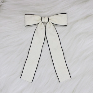 Detailed close-up of cream bow hair clip with black trim and embossed floral fabric texture