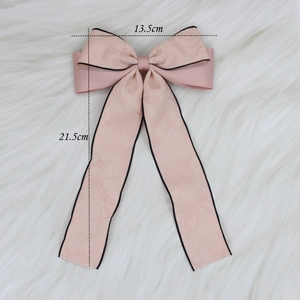 Pink bow hair clip with long ribbons and black trim on soft white plush background