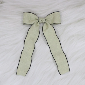 Detailed view of sage green jacquard bow hair clip with black satin piping on faux fur