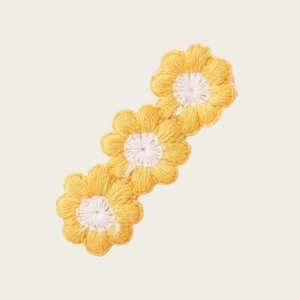 Détail de trois pinces à cheveux tournesol brodées jaune vif sur un fond beige neutre