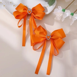 Détail de barrettes nœuds orange avec strass en cœur et longs rubans élégants