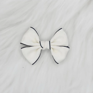Détail du nœud papillon en jacquard blanc avec liseré noir sur fond en peluche blanche