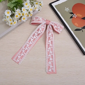 Détail de la pince à cheveux avec nœud en satin rose et broderie de dentelle blanche raffinée