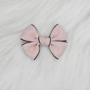 Détail d'un nœud papillon en jacquard rose avec liseré noir sur fond en peluche blanche