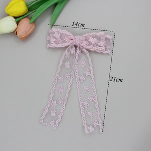 Pink lace bow hair clip with floral embroidery and long ribbons on a clean grey background