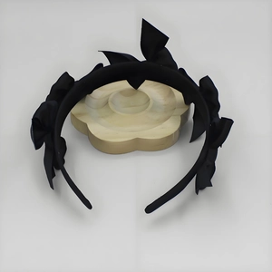 Detail view of black satin headband with multiple 3D bows on a wooden display stand