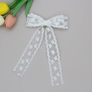 Macro detail of ivory lace bow hair clip showing intricate floral embroidery and streamers
