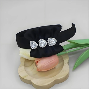 Close-up of black satin headband featuring a silk bow and three heart-shaped rhinestones