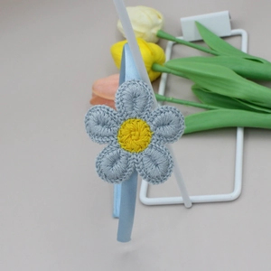 Detalle de diadema de ganchillo azul claro con flores de girasol tejidas en amarillo y gris