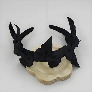 Detailed view of black satin headband with three large bows on a wooden display stand