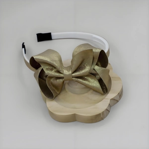 Dettaglio di un cerchietto elegante con fiocco in metallo dorato su telaio bianco