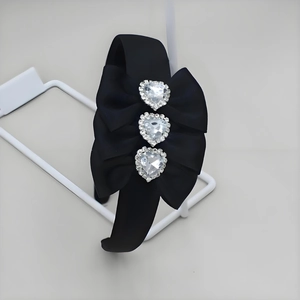 Close-up of heart-shaped rhinestones on black satin headband with large bow detail